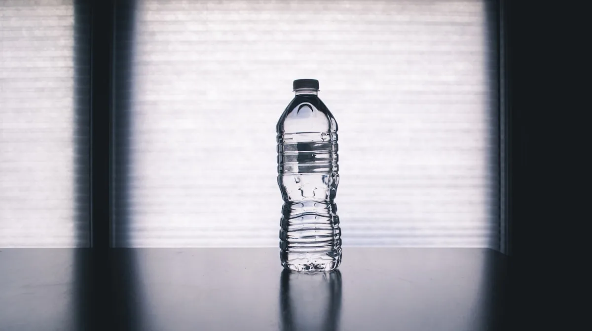 Clear water bottle with fruit slices beside it on a light background