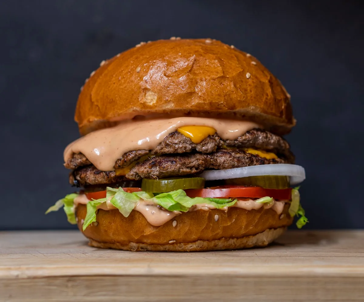 Close-up of a large beef burger with lettuce, tomato, and pickles on a sesame bun
